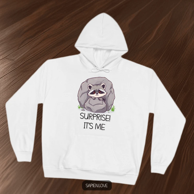 Funny bipedal raccoon character peeking from behind a large rock on a hoodie, offering warmth and humor.